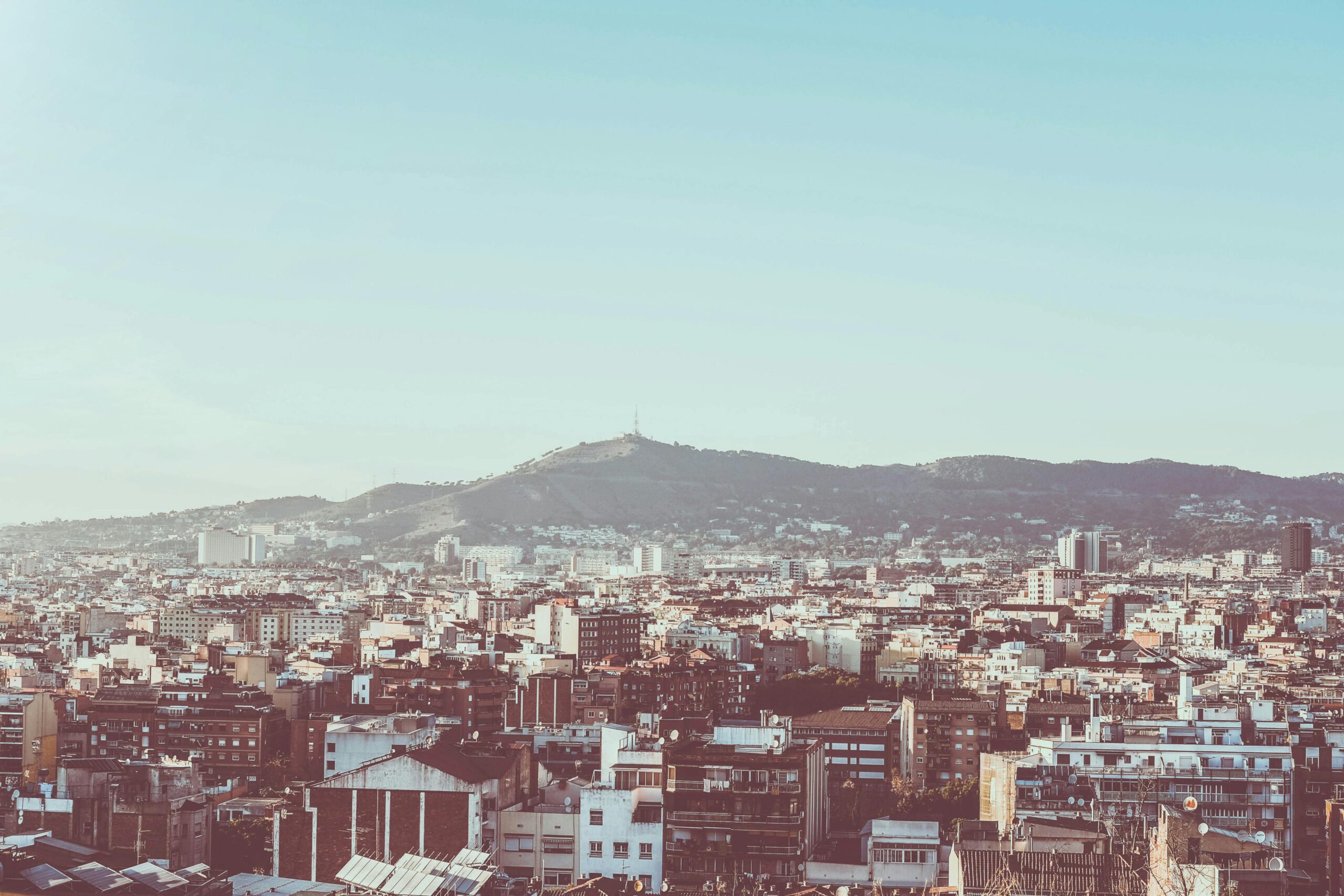 A panoramic view of Barcelona's urban landscape with Montjuïc in the background under clear skies.