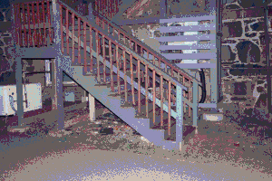 A set of wooden stairs at night leading into a cobblestone building, behind it is an air conditioning unit and some pipes. Image has been heavily compressed.