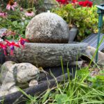 a stone rabbit statue and a small stone fountain in a flower garden